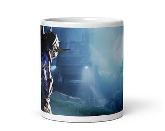 May include: White ceramic mug featuring a futuristic warrior figure in a detailed, dark-colored suit with sharp angles and metallic accents. The background shows a sci-fi landscape with a bright, glowing orb.