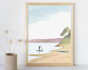 Könnte beinhalten: Ein Aquarellbild einer Strandszene mit einer Person, die im Wasser paddelt, und einem Kajak am Ufer. Das Bild ist in einem hellen Holzrahmen gerahmt.