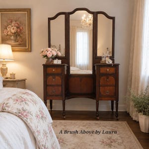 May include: A dark wood vanity table featuring a tri-fold mirror, six drawers with metal pulls, and slender legs. The piece is positioned in a room with a floral bedspread and a rug displaying the text A Brush Above by Laura.