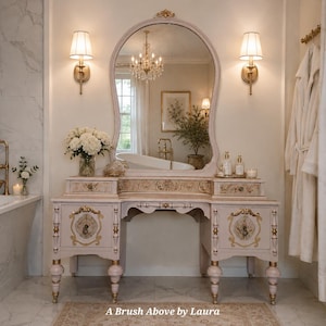 May include: A light pink vanity table with gold-painted accents, featuring two side cabinets, two drawers, and a large arched mirror. The piece is adorned with floral patterns on the drawer fronts and cabinet doors, supported by turned legs.