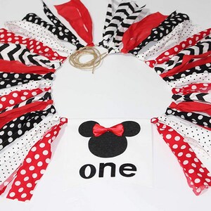 May include: A red, black, and white fabric garland with polka dots, chevron, and stripes. A white banner with a black silhouette of Minnie Mouse and the word "one" in black.