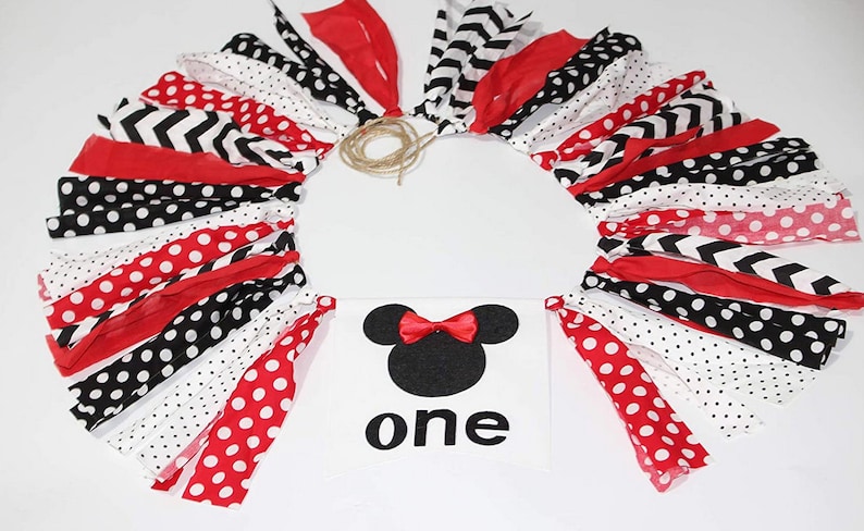 May include: A red, black, and white fabric garland with polka dots, chevron, and stripes. A white banner with a black silhouette of Minnie Mouse and the word "one" in black.