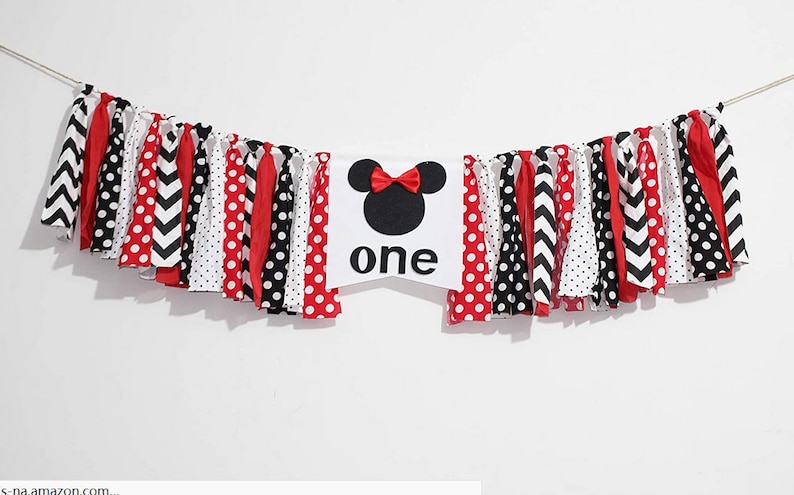 May include: A white fabric banner with a black and red Minnie Mouse head and the word "one" in black. The banner is decorated with red and white polka dot fabric, black and white chevron fabric, and red fabric.