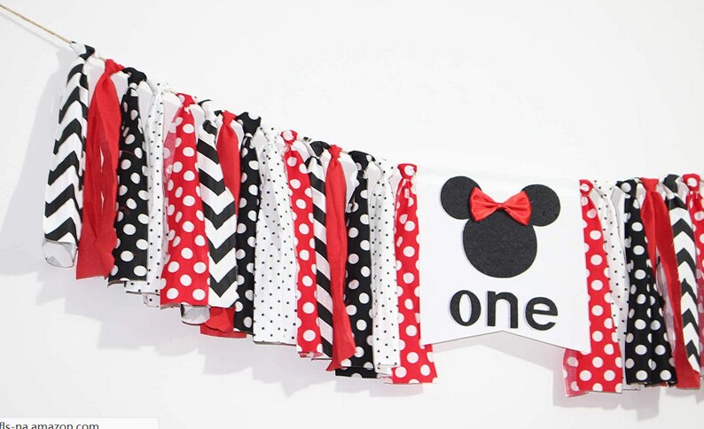 May include: A white banner with a black and red Minnie Mouse head and the word "one" in black letters. The banner is decorated with a red, black, and white fabric garland.