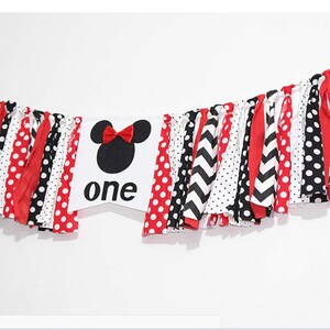 May include: A white banner with a black and red Mickey Mouse head and the word "one" in black. The banner is decorated with red, black, and white fabric strips.