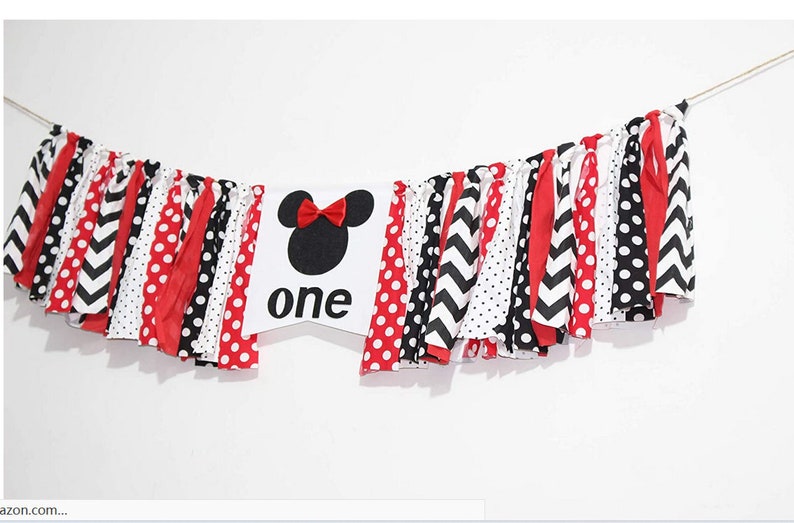 May include: A white banner with a black and red Mickey Mouse head and the word "one" in black. The banner is decorated with red, black, and white fabric strips.