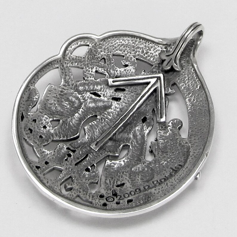 May include: Silver pendant featuring the Sagittarius zodiac sign in a Celtic knot design. The back of the pendant is engraved with the year 2009 and the artist's initials.