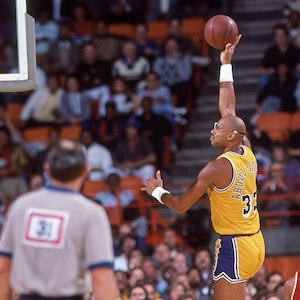 May include: A basketball player wearing a yellow and purple jersey with the number 33 and the name "ABDUL-JABBAR" on the back, jumps to shoot a basketball.