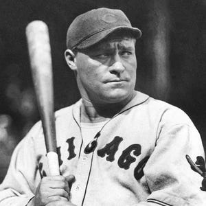 May include: Black and white photograph of a baseball player holding a bat. He wears a cap and a jersey with the word "Chicago" across the chest. The image is a vintage portrait, likely from the early 20th century.