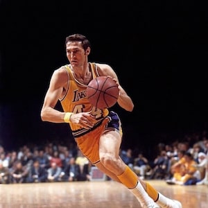 May include: A basketball player wearing a yellow and purple jersey with the word "Lakers" on it, dribbling a basketball. The player is wearing white socks and white sneakers.