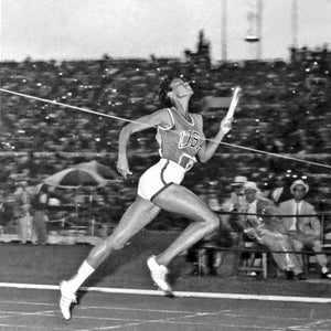 May include: Black and white photo of a track and field athlete in mid-sprint, holding a baton. The athlete wears a USA jersey and white shorts, running towards the finish line. Spectators fill the background.