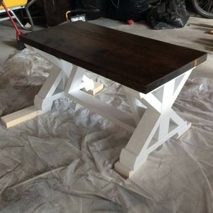 May include: A dark brown wooden table top with a white painted X-shaped base. The table is sitting on a white drop cloth.