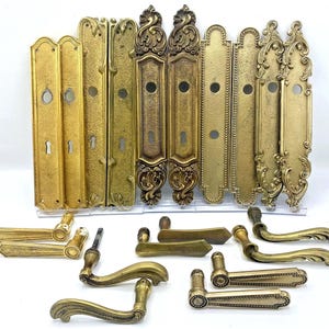 Peut inclure: Une collection de quincaillerie de porte en laiton comprenant dix plaques de propreté rectangulaires avec divers bords décoratifs et trous de serrure, ainsi que huit poignées de porte assorties de formes variées, avec des volutes et finitions lisses.