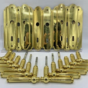 Peut inclure: Un ensemble de quincaillerie de porte en laiton poli comprenant plusieurs plaques de propreté rectangulaires aux extrémités arrondies avec entrées de clé, assorties à des poignées de porte cannelées en métal brillant.