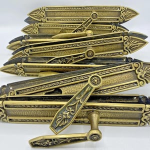 Peut inclure: Ensemble de poignées de porte anciennes en laiton. Les poignées présentent un design orné avec des motifs floraux et géométriques. Les poignées sont de couleur or chaud et semblent être en métal. Les poignées sont empilées les unes sur les autres.