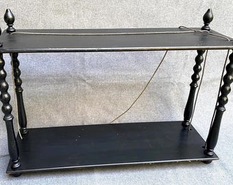 May include: Black, two-tiered shelf with decorative turned legs and finials. The shelf has a rectangular top and bottom, connected by four turned legs. A thin metal chain is strung across the top. The shelf is painted black.