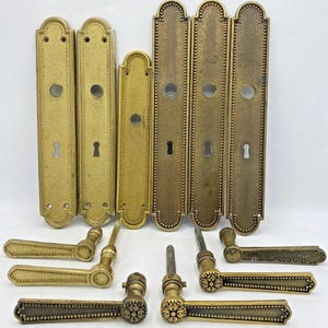 以下が含まれることがあります： キーホールと装飾的なレバーハンドルを備えた、アンティーク真鍮製のドアハードウェアのコレクション。 ハードウェアは、暖かく、古びた風合いのヴィンテージな外観です。 ドアプレートの長さは約25cmです。