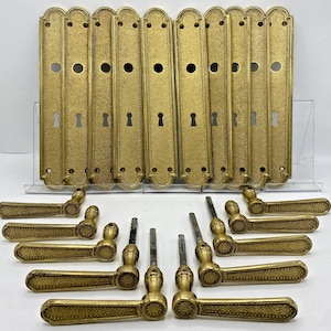 Peut inclure: Un ensemble de dix plaques de porte rectangulaires en laiton avec une finition texturée, chacune dotée d'un trou circulaire central et d'une entrée de clé. Dix poignées de porte assorties en laiton avec une prise texturée et une tige métallique.