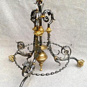 Könnte beinhalten: Verzierter Kronleuchter aus schwarzem und goldenem Metall mit dekorativem Design. Der Kronleuchter hat eine schalenförmige Oberseite und drei geschwungene Arme mit dekorativen Akzenten. Die Basis hat ein gedrehtes Metalldesign.