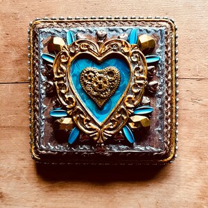 May include: A decorative heart-shaped box with a gold frame and a blue and gold interior. The box is adorned with gold and blue embellishments.