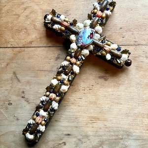 May include: A wooden cross decorated with seashells, small pieces of glass, and a blue and white agate stone in the center.