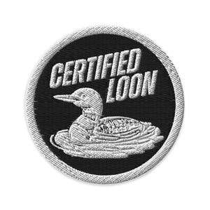 Può includere: Una toppa ricamata circolare con sfondo nero e bordo bianco. Il design raffigura un colimbo bianco che nuota nell'acqua, accompagnato dal testo bianco "CERTIFIED LOON" posizionato sopra l'uccello in un carattere grassetto senza grazie.