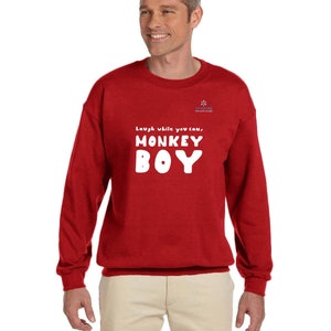 May include: A red sweatshirt with the text "Laugh while you can, MONKEY BOY" in white block letters. The sweatshirt has long sleeves and a crew neck. A small logo is visible on the upper right chest.