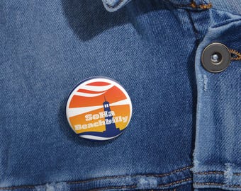 May include: A round button with a sunset and lighthouse design. The text "SoHa Beachbilly" is printed on the button.