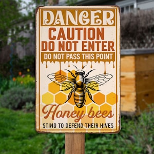 May include: A rectangular metal sign with a distressed finish, featuring a bee illustration and text. The sign reads "DANGER CAUTION DO NOT ENTER DO NOT PASS THIS POINT Honey bees STING TO DEFEND THEIR HIVES". The sign is mounted on a wooden post.