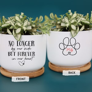 May include: Two white ceramic planters with green plants, each on a wooden saucer. One planter has the text "NO LONGER by our side BUT FOREVER in our heart" and a paw print heart. The other has a paw print design with the name "Molly".