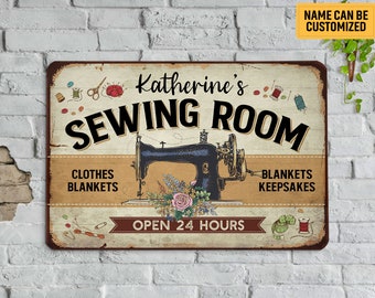 May include: A vintage-style metal sign with the text "Katherine's Sewing Room." The sign features a black sewing machine, spools of thread, and the words "Clothes, Blankets, Keepsakes." The sign also says "Open 24 Hours."