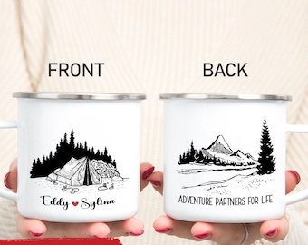 May include: White enamel camping mugs with black illustrations. One mug features a tent and the names "Eddy" and "Sylina." The other mug shows a mountain scene with the text "Adventure Partners for Life."