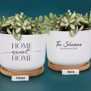 May include: Two white ceramic planters with bamboo saucers, each holding greenery. One planter reads "HOME sweet HOME," the other "The Johnsons Established 2022." The front and back labels are visible.