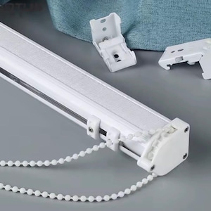 May include: White window blind track system with a beaded chain and mounting brackets. The track has a textured fabric insert and is designed for easy installation. The components are made of durable plastic and metal.