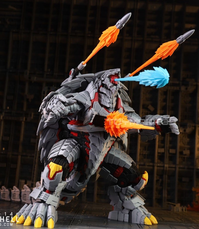 Op de afbeelding: Een grijs en rood robot speelgoed met een dinosaurusachtig ontwerp. De robot heeft meerdere oranje en blauwe projectielwapens. De robot staat op een grijs oppervlak.