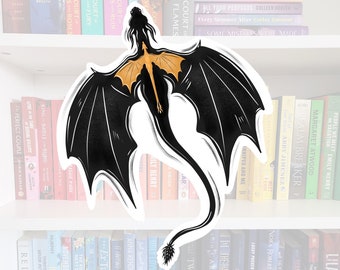Pode incluir: Um adesivo de dragão preto e dourado com as asas abertas, voando sobre um fundo branco. O dragão tem uma cauda longa e um focinho pontudo. O adesivo está numa estante com muitos livros.