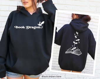 Puede incluir: Sudadera con capucha negra con un gráfico blanco de un dragón volando fuera de un libro y el texto "Book Dragon" en la parte delantera. La parte posterior de la sudadera presenta un gráfico blanco de un libro con dragones volando fuera de él.