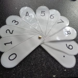 May include: A white paper fan with numbers 0 through 9 printed on each section.