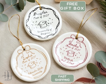 May include: Three round white ceramic ornaments with gold hanging strings. Each features a graduation cap illustration, confetti, and personalized text including names, Class of 2027, and school names: University of Arizona, Colorado State University, and Westside High School.