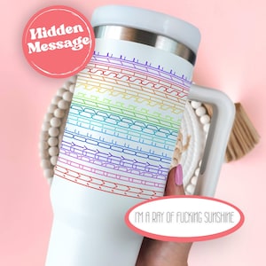 May include: White travel mug with a rainbow pattern and the text "I'M A RAY OF FUCKING SUNSHINE". The mug has a white lid and a stainless steel interior. A pink circle with the words "Hidden Message" is also visible.