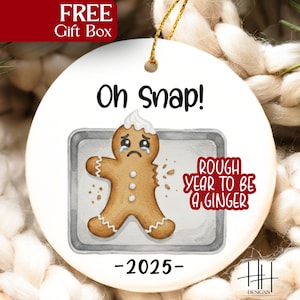 May include: A white ceramic Christmas ornament with a distressed gingerbread man design. The ornament features the text "Oh Snap!" and "Rough Year to be a Ginger" with the year "-2025-". A gold string is attached for hanging.