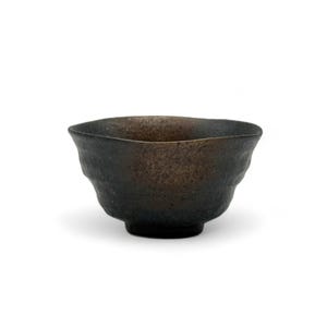 以下が含まれることがあります： 表面がざらざらしていて、不均一な、小さな濃い茶色の陶器のボウル。ボウルは丸みを帯びた形をしていて、縁が少し広がっています。