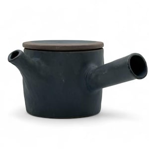 May include: A dark blue ceramic teapot with a lid. The teapot has a spout on one side and a handle on the other. The lid is a contrasting brown color. The teapot is likely handmade and has a rustic appearance.