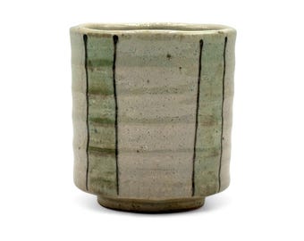 May include: A small, white ceramic cup with green and black stripes. The cup has a rounded bottom and a slightly flared rim.