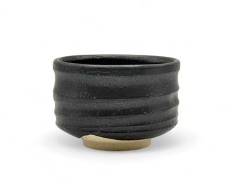 May include: A black ceramic teacup with a textured, wavy design. The cup has a light brown base.