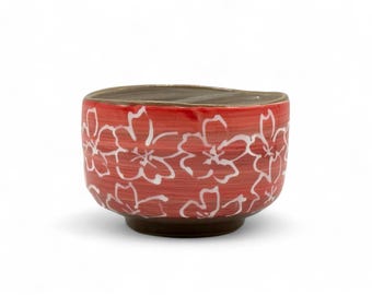 May include: A red ceramic bowl with a white floral design. The bowl has a slightly rounded shape and a brown rim.