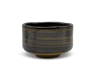 May include: A dark brown and black ceramic tea bowl with a striped pattern. The bowl has a slightly irregular shape and a rounded bottom.