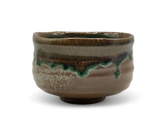 May include: A handcrafted ceramic bowl with a textured surface. The bowl features a brown base with a green and brown glaze that drips down the sides. The bowl is designed for serving food.