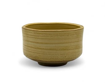 Può includere: Ciotola in ceramica marrone chiaro con un motivo a righe orizzontali strutturato. La ciotola ha una base arrotondata e un bordo leggermente squadrato. Il colore neutro e il design semplice la rendono adatta a vari usi.