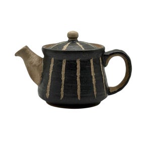 Puede incluir: Tetera de cerámica hecha a mano, cuerpo negro con rayas verticales beige. El pico, el asa y la tapa son beige. La tapa tiene un pequeño pomo. Ideal para servir té.